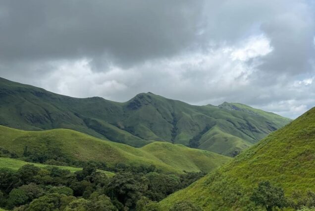 Scenic view of the Kudremukha peak in Karnataka's Western Ghats, featuring rolling green hills, mist-covered valleys, and dense forests during a trek